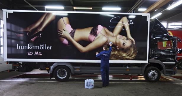 Ein Mercedes-Benz-Mitarbeiter reinigt einen LKW mit einer Hunkemöller-Werbung mit Sylvie Meis.
