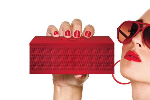 Eine Frau mit roter Sonnenbrille hält einen roten JamBox Lautsprecher in der Hand.