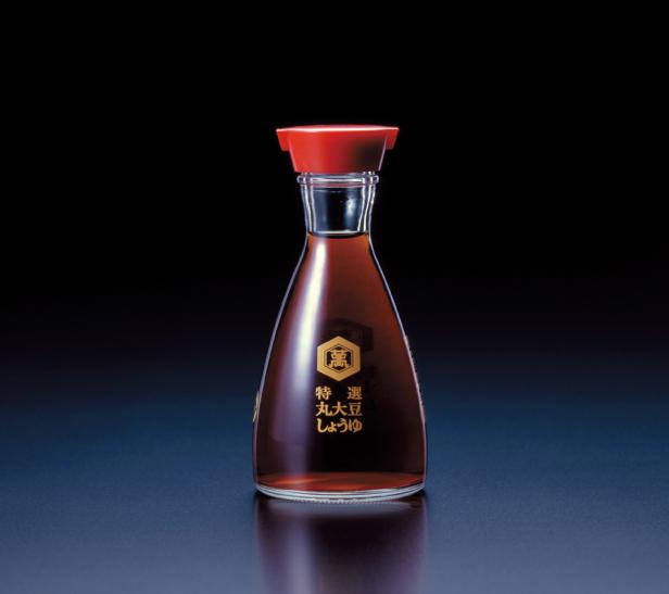 Eine Flasche Sojasauce mit rotem Verschluss vor einem dunklen Hintergrund.