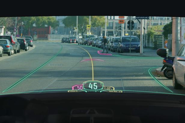 Die Windschutzscheibe eines Autos zeigt eine Augmented-Reality-Navigation, während eine Person die Straße überquert.