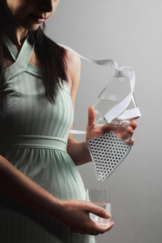 Eine Frau gießt Wasser aus einer ungewöhnlichen Karaffe in ein Glas.