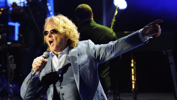 Ein Sänger mit blonden Locken und Sonnenbrille tritt auf einer Bühne auf.