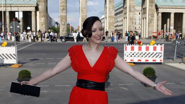 Eine Frau in einem roten Kleid posiert vor dem Brandenburger Tor in Berlin.