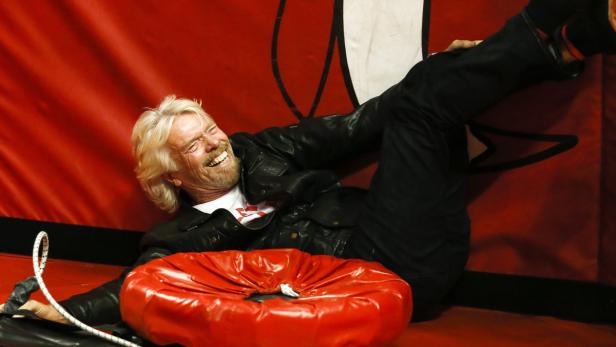 Richard Branson liegt lachend auf einer roten Matte mit einem roten Kissen.
