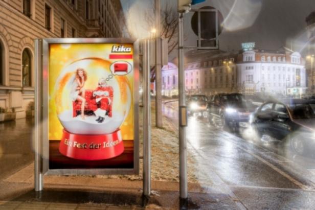 Ein Werbeplakat von Kika mit einer Schneekugel und dem Slogan „Ein Fest der Ideen“ steht an einer Straße.
