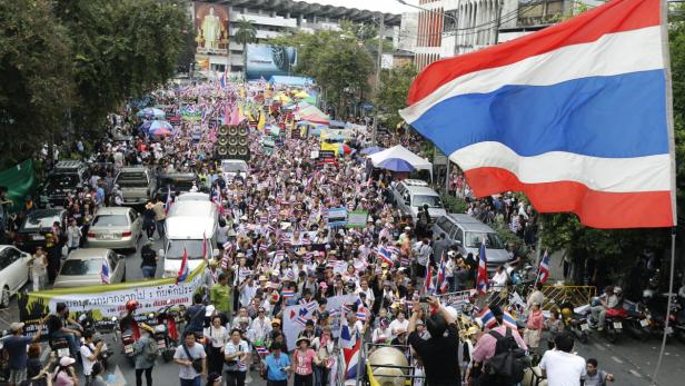 Eine große Menschenmenge demonstriert mit thailändischen Flaggen auf einer Straße.