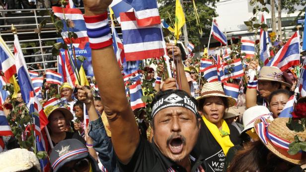Eine Menschenmenge demonstriert mit thailändischen Flaggen und erhobenen Fäusten.