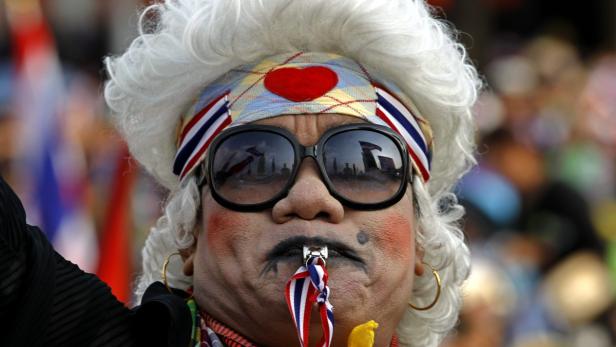 Ein Demonstrant mit weißer Perücke, Stirnband und übergroßer Sonnenbrille bei einer Kundgebung in Thailand.