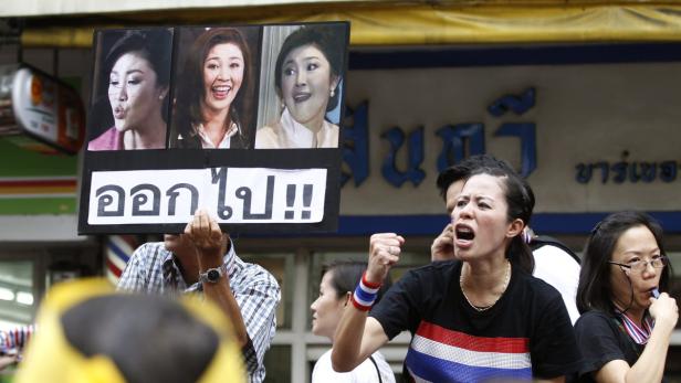 Eine Frau demonstriert mit erhobener Faust und einem Schild mit Fotos von Yingluck Shinawatra.