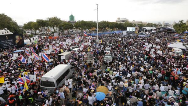 Eine große Menschenmenge mit thailändischen Flaggen versammelt sich auf einer Straße.