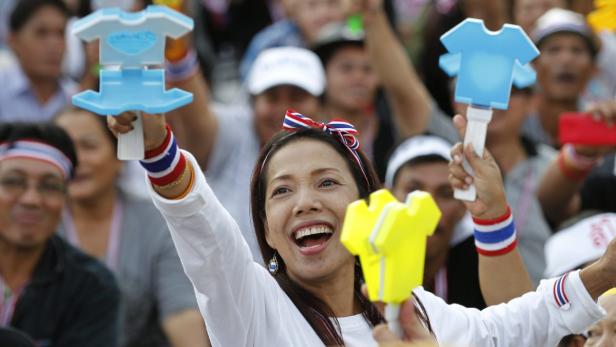 Eine lächelnde Frau hält T-Shirt-förmige Schilder in den thailändischen Nationalfarben hoch.