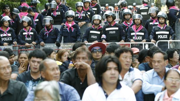Eine Menschenmenge wird von Polizisten mit Helmen und Schutzwesten bewacht.