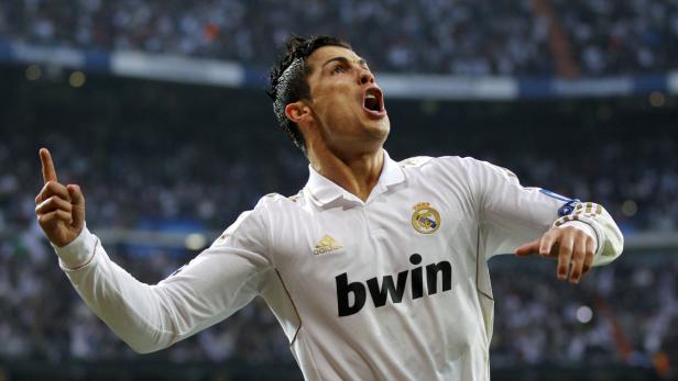 Cristiano Ronaldo jubelt in einem weißen Real Madrid Trikot mit ausgestrecktem Arm.