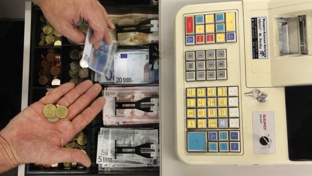 Eine geöffnete Kasse mit Euro-Münzen und -Scheinen wird von Händen sortiert.