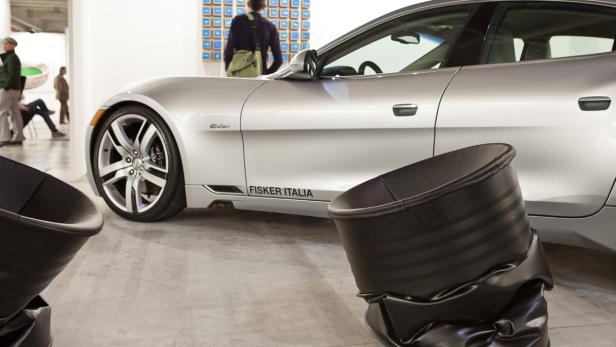 Ein silberner Fisker Karma steht in einer Ausstellungshalle neben schwarzen Stühlen.