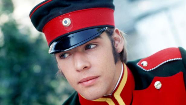 Ein junger Mann in einer roten Militäruniform und Mütze blickt nach links.