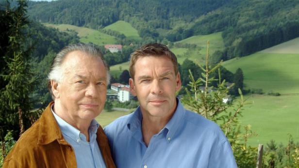 Zwei Männer stehen vor einer grünen Hügellandschaft.