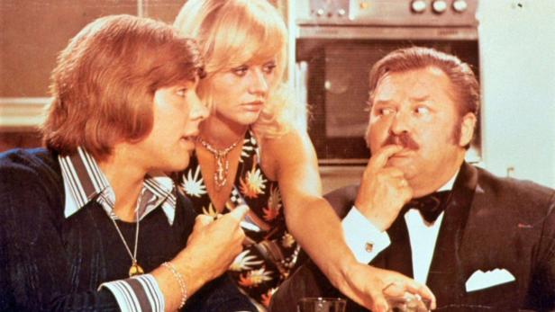 Drei Personen in Kleidung der 1970er Jahre unterhalten sich.