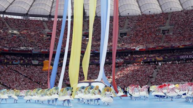 Eine Eröffnungszeremonie mit Tänzern und bunten Bändern in einem vollbesetzten Stadion.