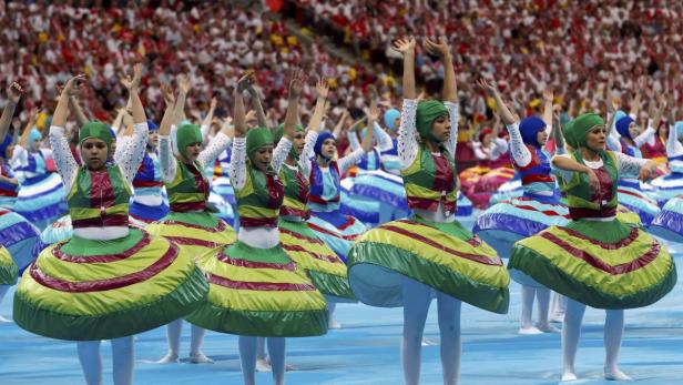 Eine Gruppe von Tänzerinnen in farbenfrohen Kostümen tritt vor einer Zuschauermenge auf.