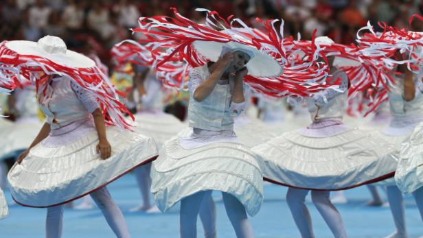 Eine Gruppe von Tänzerinnen in weißen Kostümen und Hüten mit roten und weißen Bändern tritt auf.