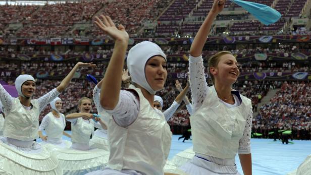 Eine Gruppe junger Frauen in weißen Kostümen tanzt in einem Stadion.