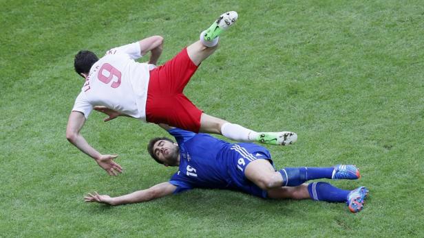 Ein Fußballspieler in Rot und Weiß fällt über einen am Boden liegenden Spieler in Blau.