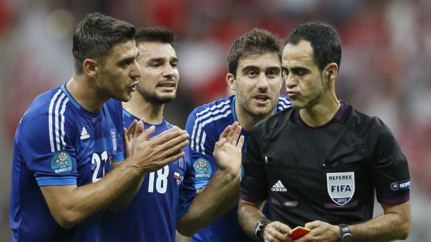 Ein Schiedsrichter diskutiert mit mehreren griechischen Fußballspielern während eines Spiels.