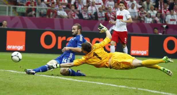 Ein Fußballspieler in Blau grätscht, während ein Torwart in Gelb versucht, den Ball abzuwehren.
