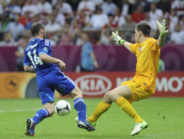 Ein Fußballspieler mit der Nummer 14 schießt den Ball, während ein Torwart versucht, ihn abzuwehren.