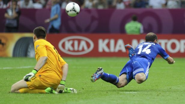 Ein Fußballspieler schießt den Ball, während der Torwart auf dem Rasen kniet.