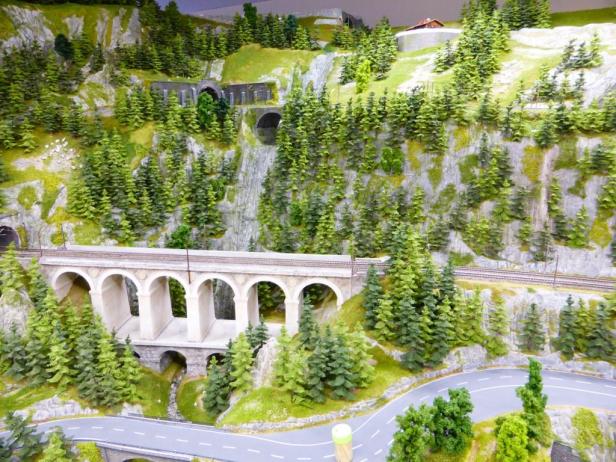 Eine Miniaturlandschaft mit Bergen, Tunnels, einer Eisenbahnbrücke und einer gewundenen Straße.
