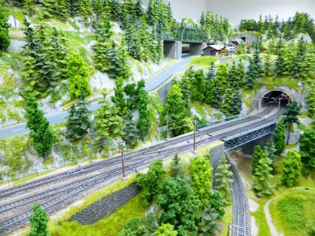 Eine Modelleisenbahnlandschaft mit Tunnel, Brücken und vielen Bäumen.