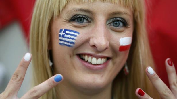 Eine Frau mit aufgemalten Flaggen von Griechenland und Polen im Gesicht lächelt.