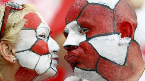 Zwei Fußballfans mit rot-weißer Gesichtsbemalung stehen einander gegenüber.