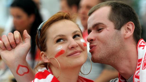 Ein Mann gibt einer Frau mit rot-weißen Wangenmalereien einen Kuss.