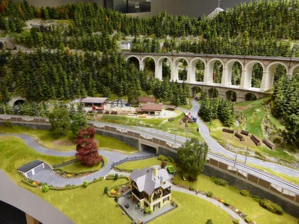 Eine Miniaturlandschaft mit einem Haus, einer Eisenbahnstrecke und einer Bogenbrücke.
