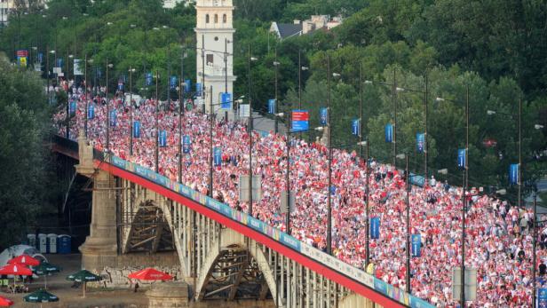 Eine Menschenmenge in Rot und Weiß überquert eine Brücke in Warschau.