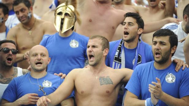 Eine Gruppe griechischer Fußballfans jubelt, einige tragen blaue T-Shirts und griechische Flaggen.