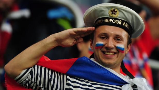 Ein lächelnder Mann mit russischer Flagge auf den Wangen grüßt in Marineuniform.