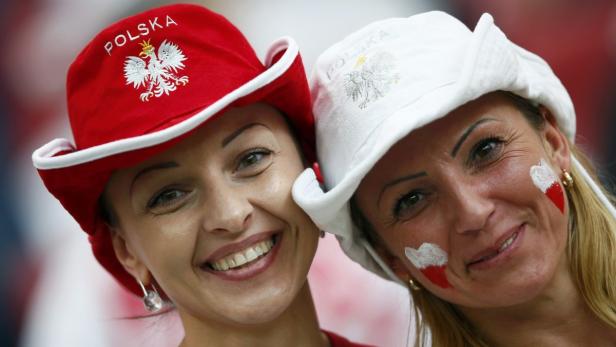 Zwei Frauen mit Hüten und Gesichtsbemalung in den polnischen Nationalfarben lächeln.