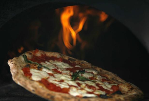 Eine Pizza mit Tomaten, Mozzarella und Basilikum wird in einem Ofen gebacken.