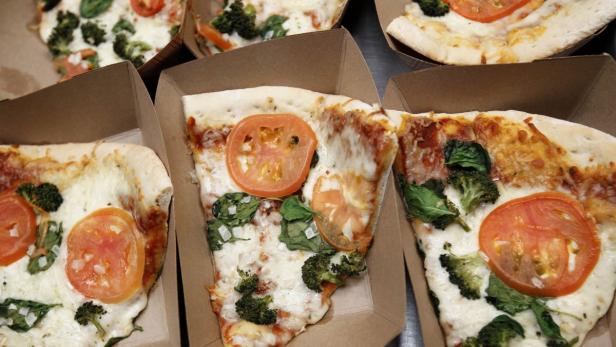 Mehrere Pizzastücke mit Tomaten, Spinat und Brokkoli in Pappkartons.