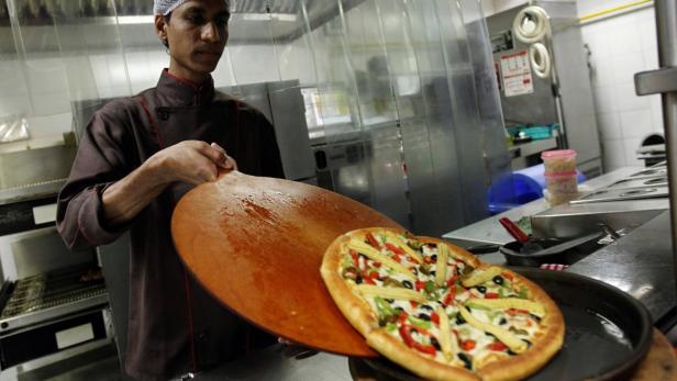 Ein Koch hält eine Pizza mit Gemüse auf einem Holzschieber.