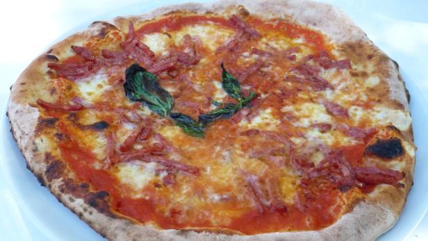 Eine Pizza mit Salami, Tomatensoße und Basilikum liegt auf einem Teller.