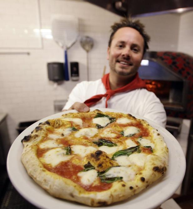 Ein Pizzabäcker präsentiert eine frisch zubereitete Pizza Margherita.