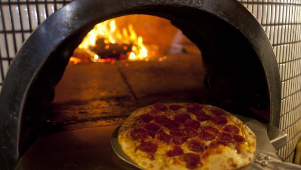 Eine Pizza mit Salami wird in einem Steinofen gebacken.