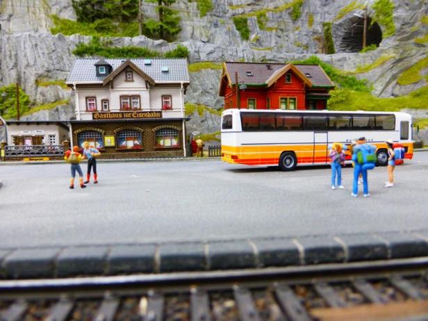 Eine Modellbahnszene mit einem Bus und dem „Gasthaus zur Eisenbahn“ vor einer Felswand.
