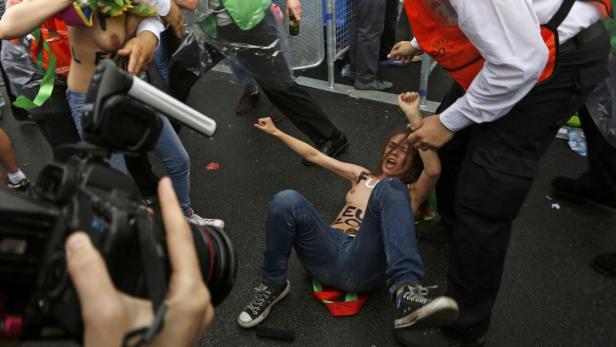 Eine Aktivistin mit aufgemalten Parolen wird von Sicherheitskräften abgeführt.