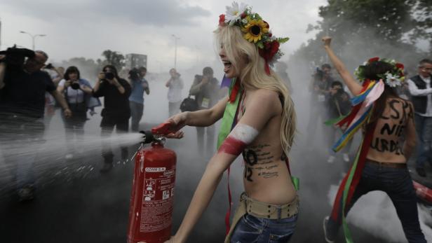 Eine Frau mit Blumenkranz sprüht mit einem Feuerlöscher in einer Menschenmenge.